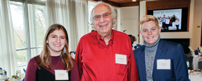 An older man in a red shirt is flanked by two younger people